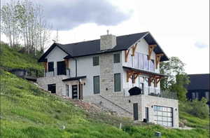 View of front facade featuring stone siding, a garage, a balcony, and a chimney
