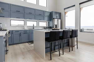 Kitchen featuring light stone countertops, gray cabinetry, a breakfast bar area, appliances with stainless steel finishes, and light wood-type flooring