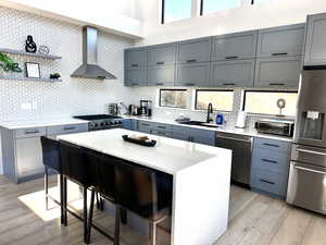 Kitchen with a kitchen breakfast bar, wall chimney range hood, decorative backsplash, light stone countertops, and stainless steel appliances