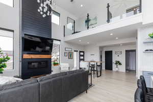 Living room with light wood-type flooring, a towering ceiling, recessed lighting, and a large fireplace