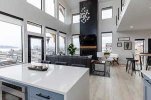 Kitchen featuring light wood-style flooring, light stone counters, a high ceiling, a kitchen island, and a large fireplace