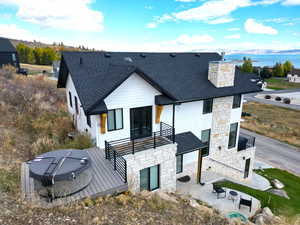 Back of property featuring stone siding, roof with shingles, a deck with water view, and a patio area