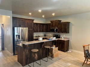 Kitchen with dark brown cabinets, stainless steel appliances, light stone counters, a textured ceiling, and light wood finished floors