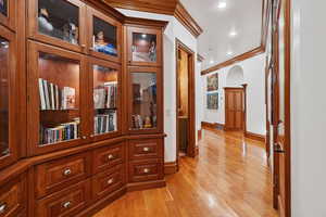 Hallway with ornamental molding, light wood-style floors, arched walkways, and recessed lighting
