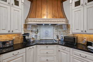 Kitchen with premium range hood, glass insert cabinets, tasteful backsplash, and black electric cooktop