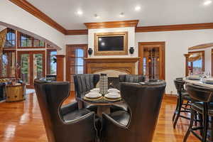 Dining room featuring a fireplace, arched walkways, crown molding, french doors, and light wood finished floors