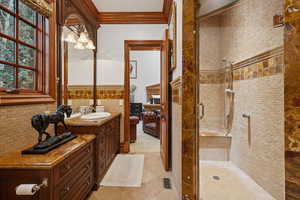 Ensuite bathroom featuring a shower stall, vanity, crown molding, tile walls, and a wainscoted wall