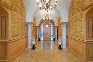 Foyer with a chandelier, arched walkways, vaulted ceiling, inlaid floor details, and a decorative wall