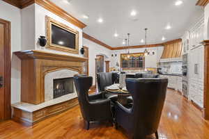 Dining area featuring arched walkways, a fireplace, light wood-style flooring, ornamental molding, and recessed lighting