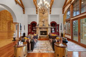 Living room featuring a towering ceiling, a high end fireplace, arched walkways, wood finished floors, and beamed ceiling