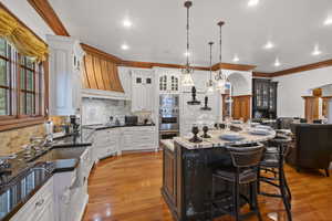 Kitchen featuring a breakfast bar, backsplash, decorative light fixtures, premium range hood, and light wood-style flooring