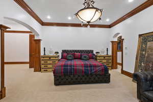 Bedroom with arched walkways, crown molding, and light colored carpet