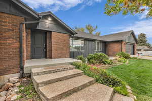 Doorway to property featuring board and batten siding, a lawn, a garage, and brick siding