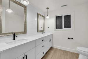 Bathroom featuring light wood-style floors, double vanity, crown molding, and tasteful backsplash