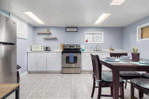 Kitchen with stainless steel appliances, light countertops, white cabinets, and open shelves