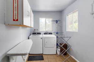 Laundry room featuring cabinet space, washing machine and clothes dryer, healthy amount of natural light, and light tile patterned floors