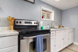 Kitchen featuring electric range, light countertops, and white cabinetry