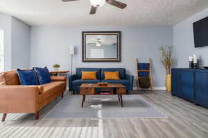 Living area featuring a ceiling fan, wood finished floors, and a textured ceiling