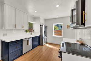 Kitchen featuring backsplash, white cabinets, blue cabinets, appliances with stainless steel finishes, and recessed lighting