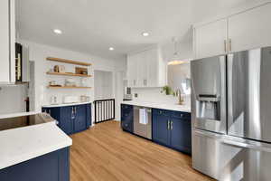 Kitchen with blue cabinetry, appliances with stainless steel finishes, white cabinets, open shelves, and light wood finished floors
