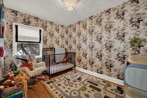 Bedroom featuring wood finished floors, wallpapered walls, a crib, and a chandelier