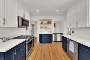 Kitchen with blue cabinets, backsplash, white cabinetry, open shelves, and recessed lighting