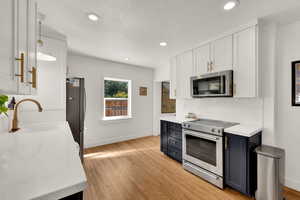 Kitchen featuring white cabinets, backsplash, stainless steel appliances, light wood-type flooring, and recessed lighting
