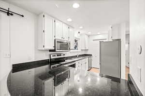 Kitchen with white cabinets, appliances with stainless steel finishes, dark stone counters, recessed lighting, and a peninsula