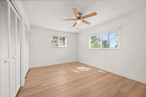 Unfurnished bedroom featuring two closets, light wood-type flooring, multiple windows, and ceiling fan