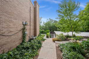 View of side of home with brick siding, a chimney, a garden, and view of scattered trees
