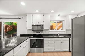 Kitchen featuring appliances with stainless steel finishes, white cabinetry, recessed lighting, dark stone counters, and light wood finished floors