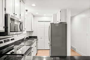 Kitchen with appliances with stainless steel finishes, white cabinets, dark stone countertops, light wood-style floors, and recessed lighting