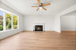 Unfurnished living room with light wood-type flooring, a premium fireplace, and a ceiling fan