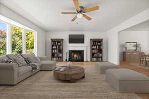 Living room with a high end fireplace, wood finished floors, and a ceiling fan