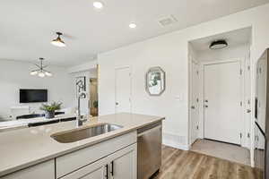 Kitchen featuring light wood-style floors, dishwasher, decorative light fixtures, white cabinets, and light stone counters