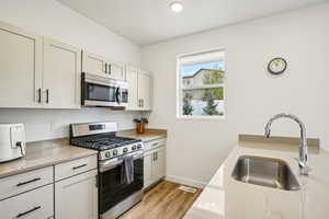 Kitchen with stainless steel appliances, light wood finished floors, light stone countertops, white cabinets, and recessed lighting