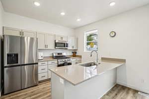 Kitchen with stainless steel appliances, light wood finished floors, a peninsula, light stone counters, and recessed lighting