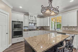 Kitchen featuring decorative light fixtures, ornamental molding, stainless steel appliances, white cabinetry, and light stone counters