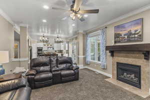 Carpeted living room featuring ornamental molding, recessed lighting, a fireplace with flush hearth, ceiling fan, and a chandelier