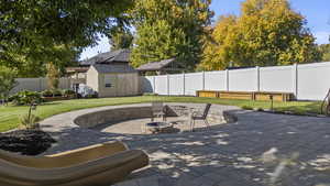 Fenced backyard featuring a storage shed, a patio area, and a fire pit
