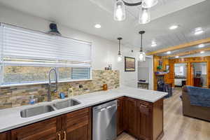 Kitchen featuring dishwasher, light stone countertops, beam ceiling, hanging light fixtures, and light wood-style flooring