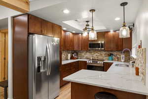 Kitchen with stainless steel appliances, tasteful backsplash, a raised ceiling, a peninsula, and pendant lighting
