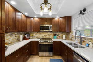 Kitchen with appliances with stainless steel finishes, light stone countertops, decorative light fixtures, tasteful backsplash, and recessed lighting