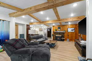 Living area featuring wood walls, beamed ceiling, light wood finished floors, recessed lighting, and a wood stove
