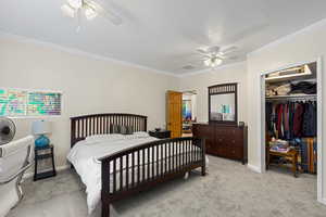 Bedroom with light carpet, ceiling fan, a closet, and ornamental molding