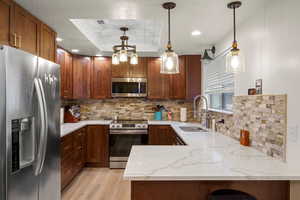 Kitchen featuring appliances with stainless steel finishes, pendant lighting, a peninsula, light stone countertops, and recessed lighting