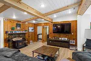 Living area with wood walls, light wood-type flooring, recessed lighting, beam ceiling, and a fireplace