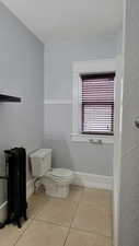 Bathroom with a textured wall, light tile patterned flooring, and radiator
