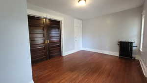 Unfurnished bedroom with radiator, a textured ceiling, dark wood-style flooring, and a closet