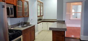 Kitchen with appliances with stainless steel finishes, light tile patterned floors, glass insert cabinets, and brown cabinets